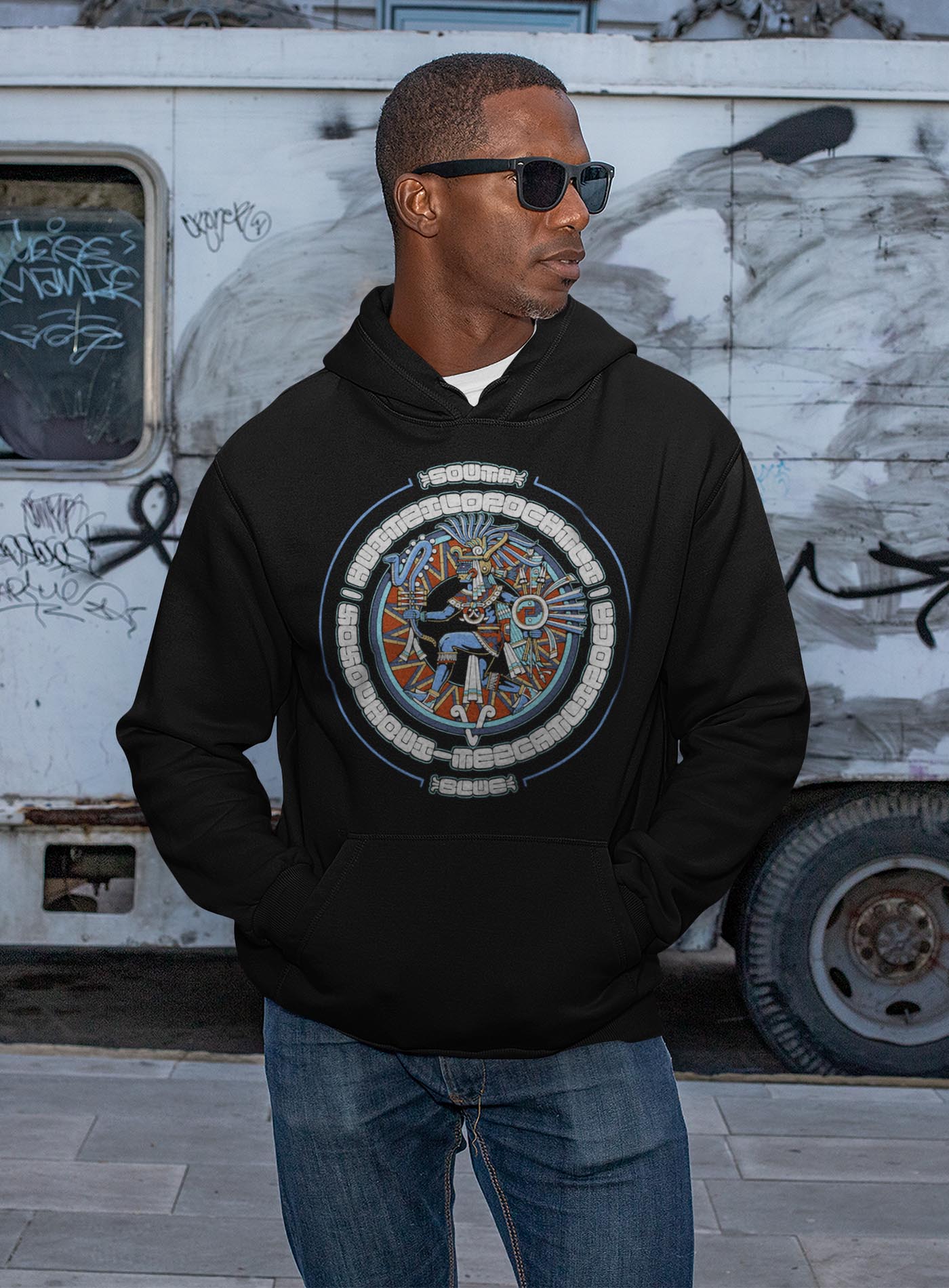 man modeling a black unisex hoodie featuring a front print of the toltec-aztec god Tezcatlipoca also known as Huitzilopochtli. Reinterpretation by Mexican illustrator G.M. Meave.