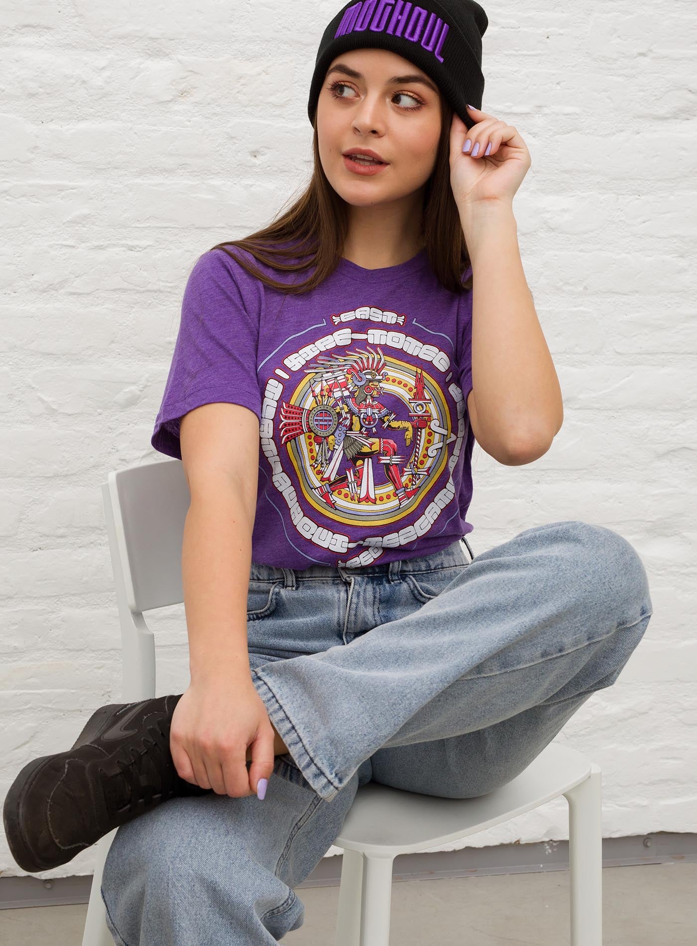 Female modeling a Heather purple unisex t-shirt featuring a front print of the toltec-aztec god Tlatlauhqui-Tezcatlipoca also known as Xipe-Totec. Reinterpretation by Mexican illustrator G.M. Meave.