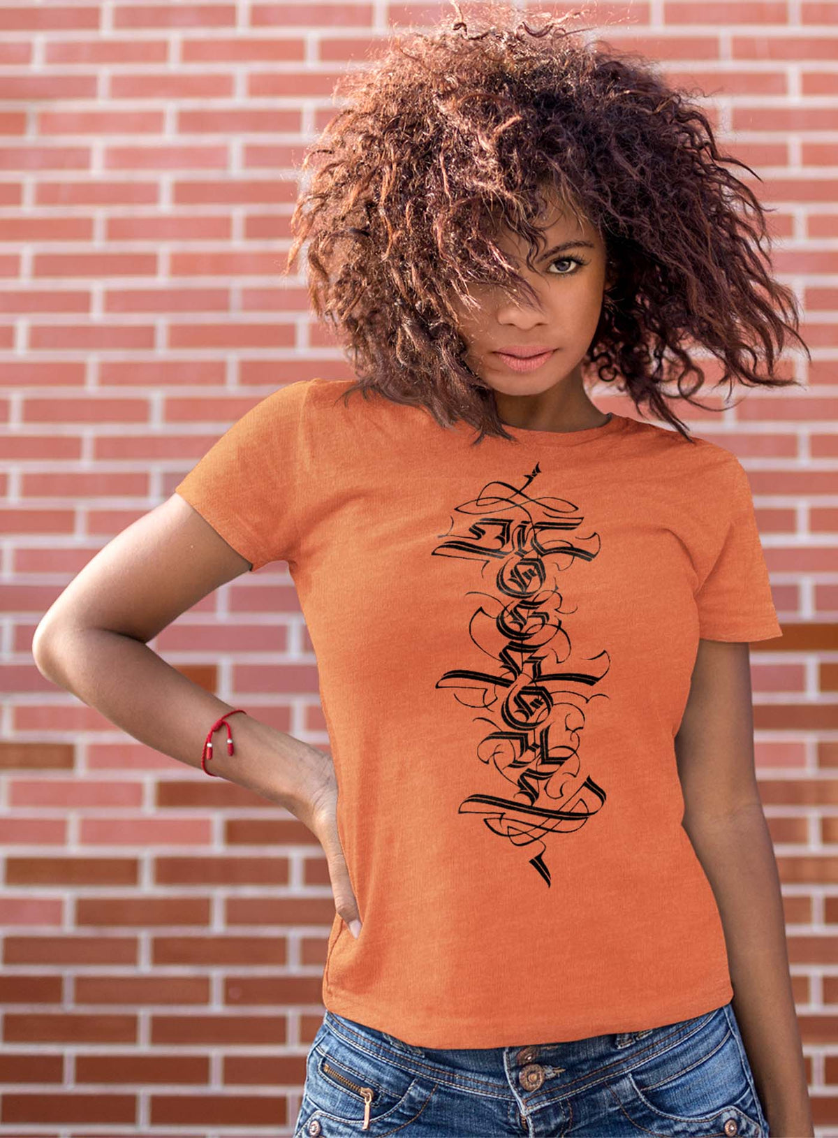 Woman modeling a Heather orange unisex t-shirt featuring a front print of a white Moghoul straight-up-gothic logo by Mexican typographer G.M. Meave.