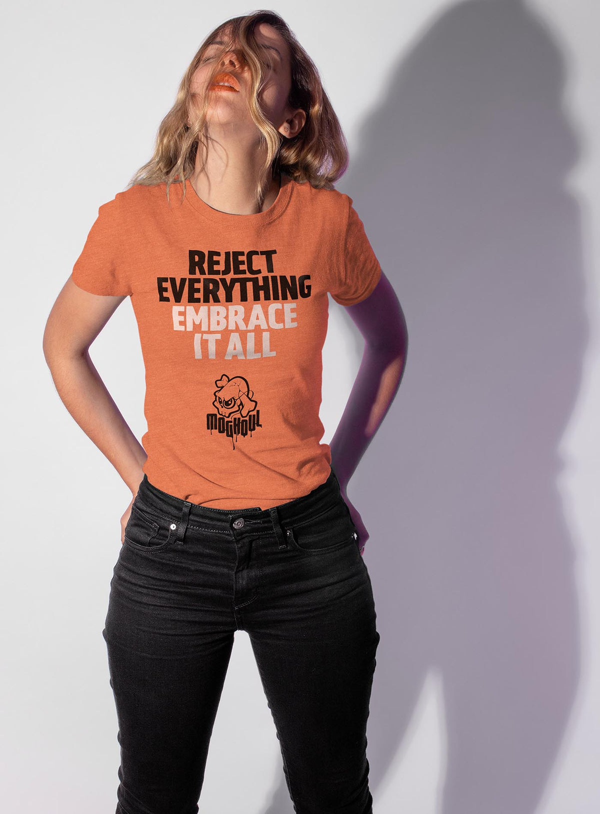 Woman modeling an Orange unisex t-shirt featuring the paradoxical phrase &quot;Reject everything, embrace it all&quot; and the moghoul logo.