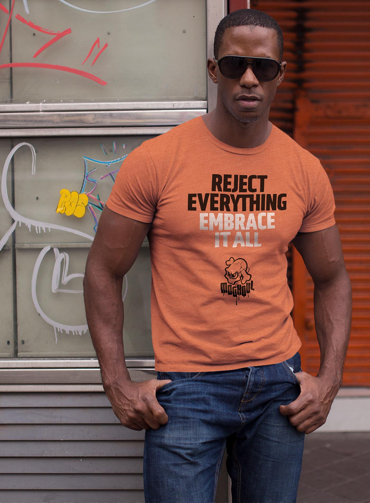 man modeling an Orange unisex t-shirt featuring the paradoxical phrase &quot;Reject everything, embrace it all&quot; and the moghoul logo.