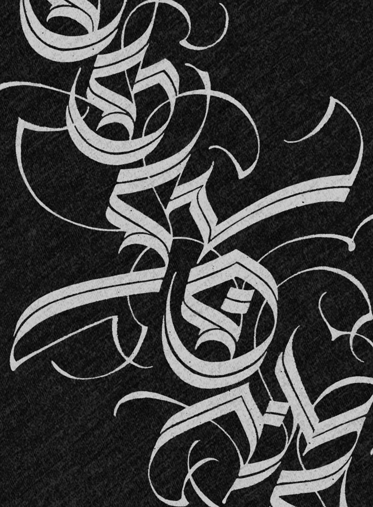 Detail of Heather black unisex t-shirt featuring a front print of a white Moghoul straight-up-gothic logo by Mexican typographer G.M. Meave.