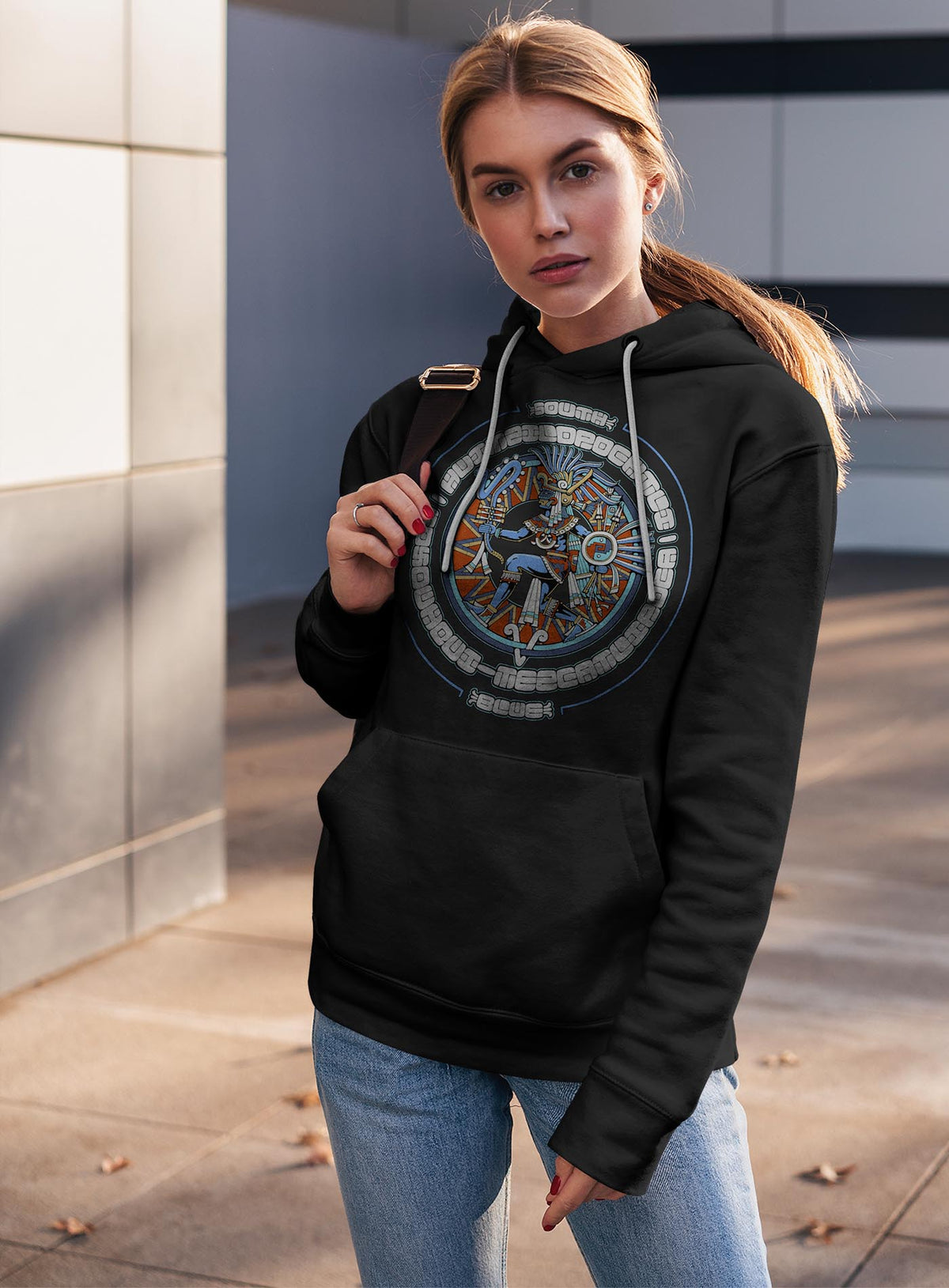 Woman modeling a black unisex hoodie featuring a front print of the toltec-aztec god Tezcatlipoca also known as Huitzilopochtli. Reinterpretation by Mexican illustrator G.M. Meave.