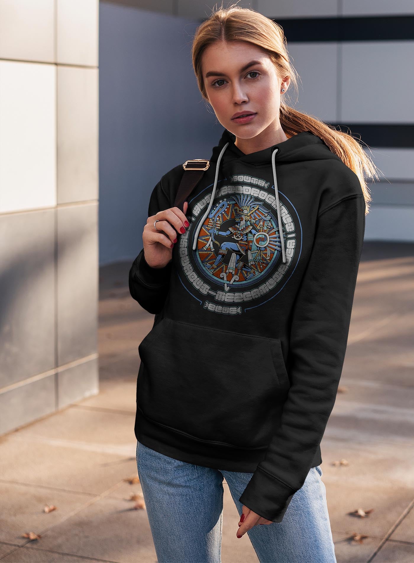 man modeling a black unisex hoodie featuring a front print of the toltec-aztec god Tezcatlipoca also known as Huitzilopochtli. Reinterpretation by Mexican illustrator G.M. Meave.