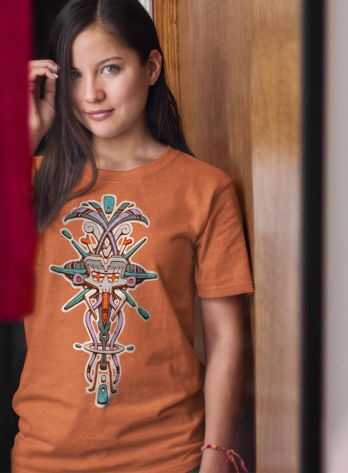 Woman modeling a Heather orange unisex t-shirt featuring a front print of Tzontecotl, the Nahua word for skull, associated with a mask that submerged the wearer into the underworld. illustrated by G.M. Meave.