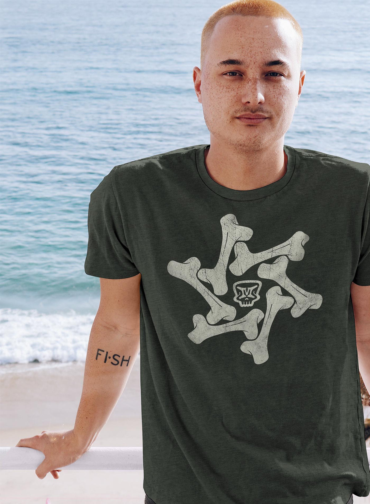 Man modeling a Heather green unisex t-shirt featuring a front print of the Moghoul symbol surrounded by a star of bones.