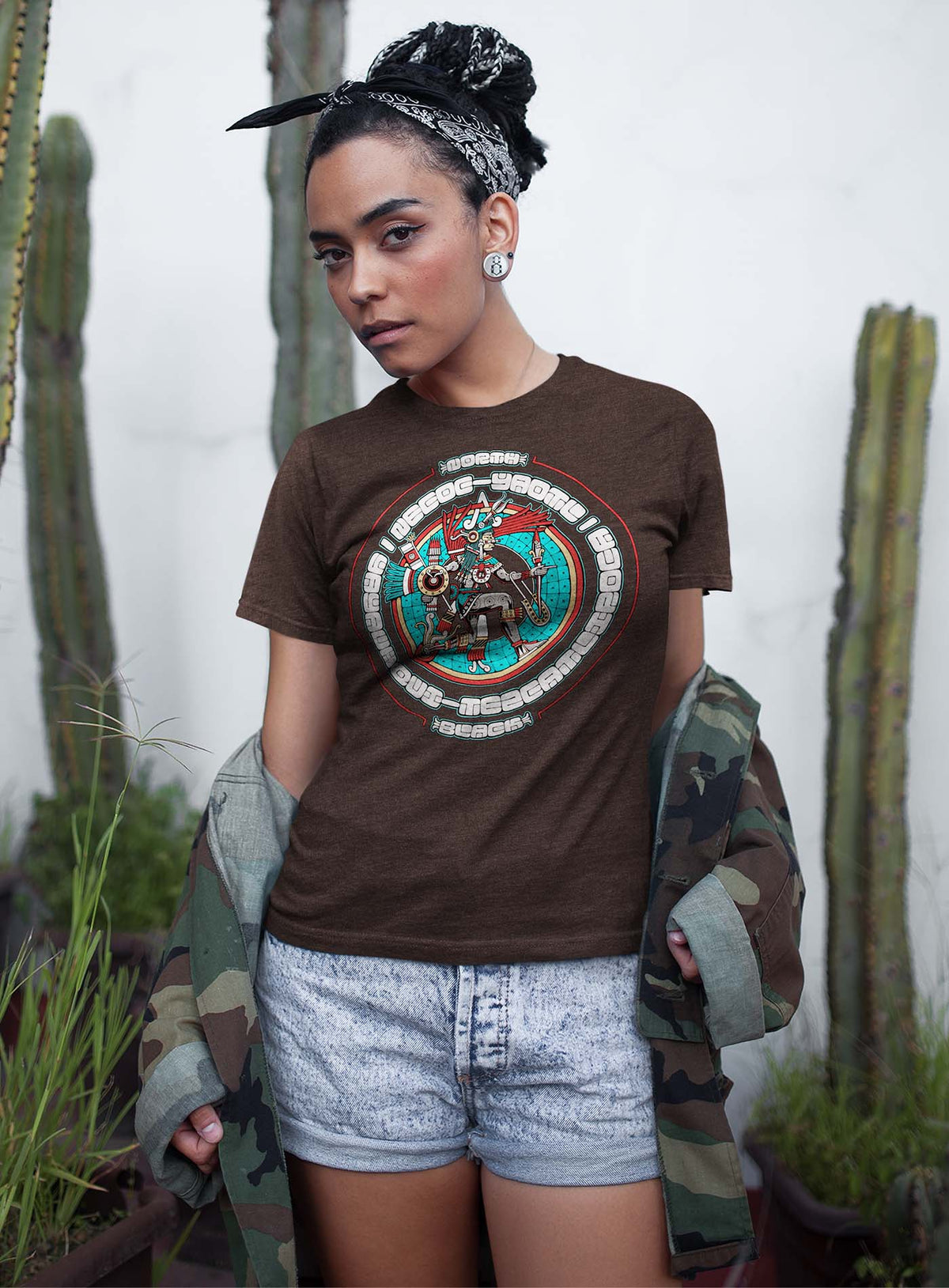 Woman modeling a Heather brown unisex t-shirt featuring a front print of the toltec-aztec god Yayauhqui-Tezcatlipoca also known as Necoc-yaotl. Reinterpretation by Mexican illustrator G.M. Meave.