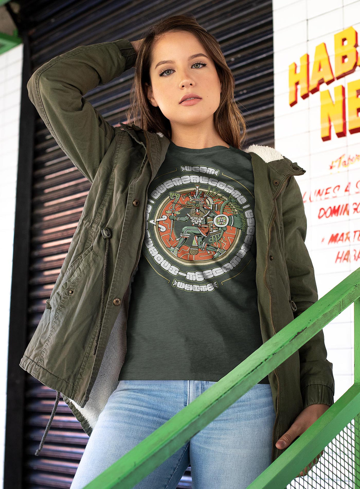 Woman modeling a Heather green unisex t-shirt featuring a front print of the toltec-aztec god Tezcatlipoca also known as Quetzalcoatl. Reinterpretation by Mexican illustrator G.M. Meave.