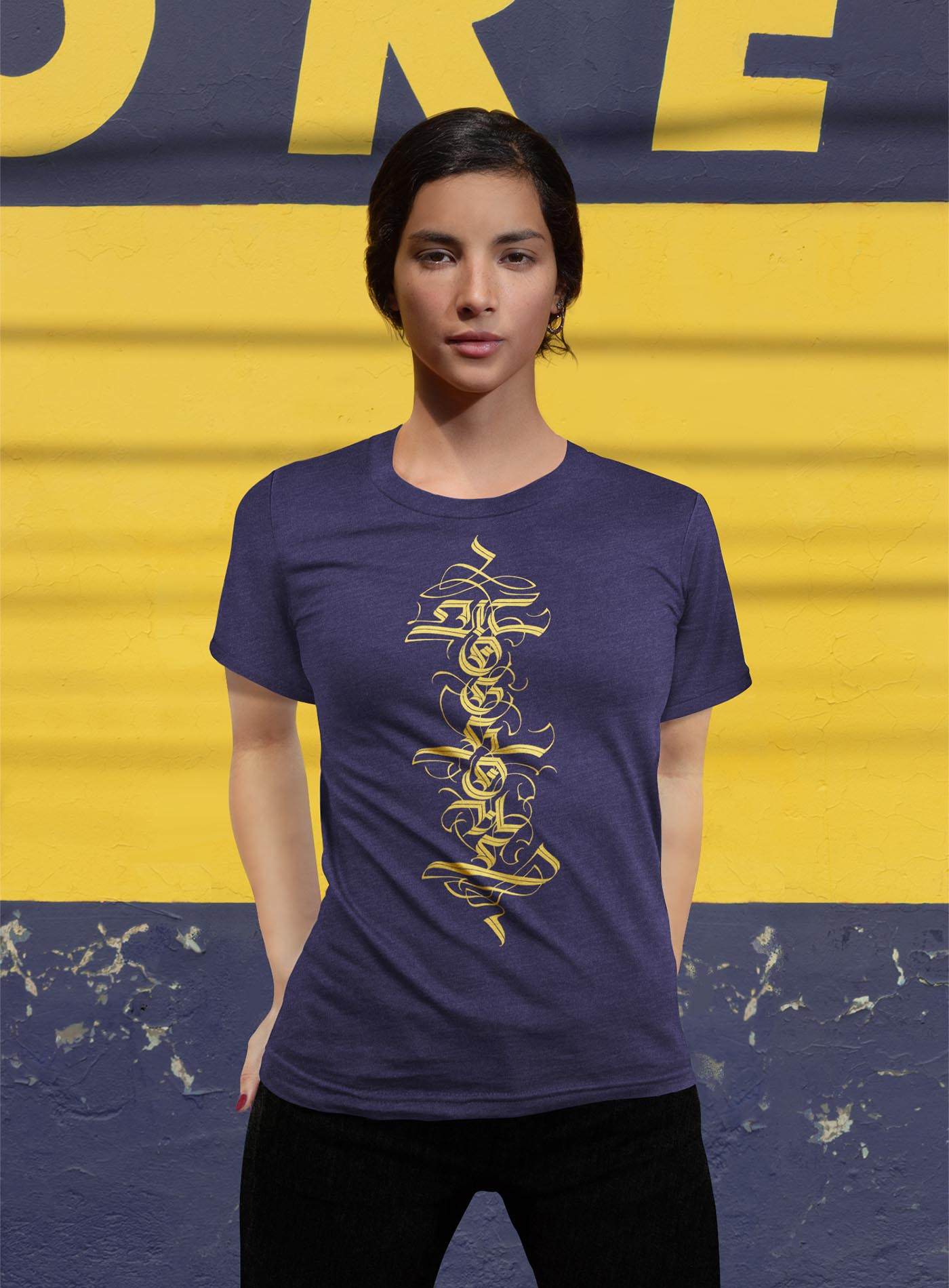 Female modeling a Heather blue unisex t-shirt featuring a front print of a white Moghoul straight-up-gothic logo by Mexican typographer G.M. Meave.