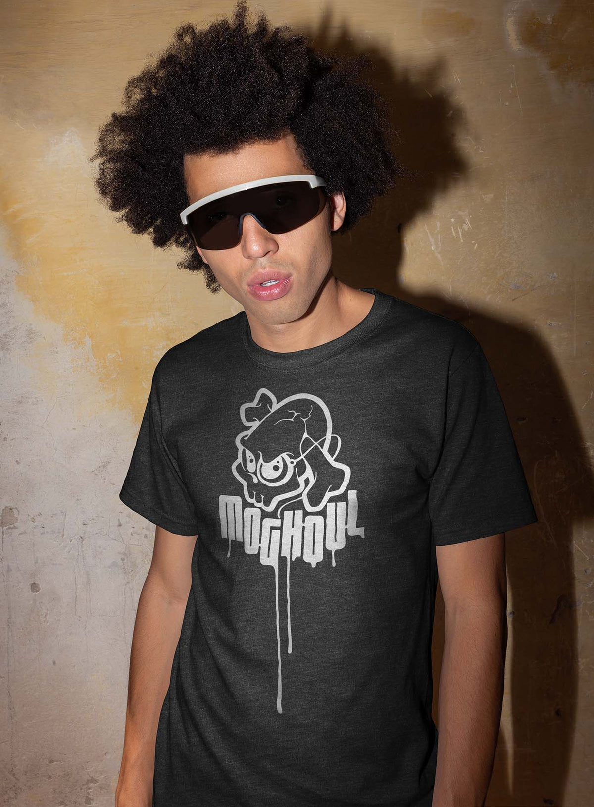 man modeling a heather grey unisex t-shirt featuring a yellow Mr. Shade Moghoul logo by G.M. Meave.