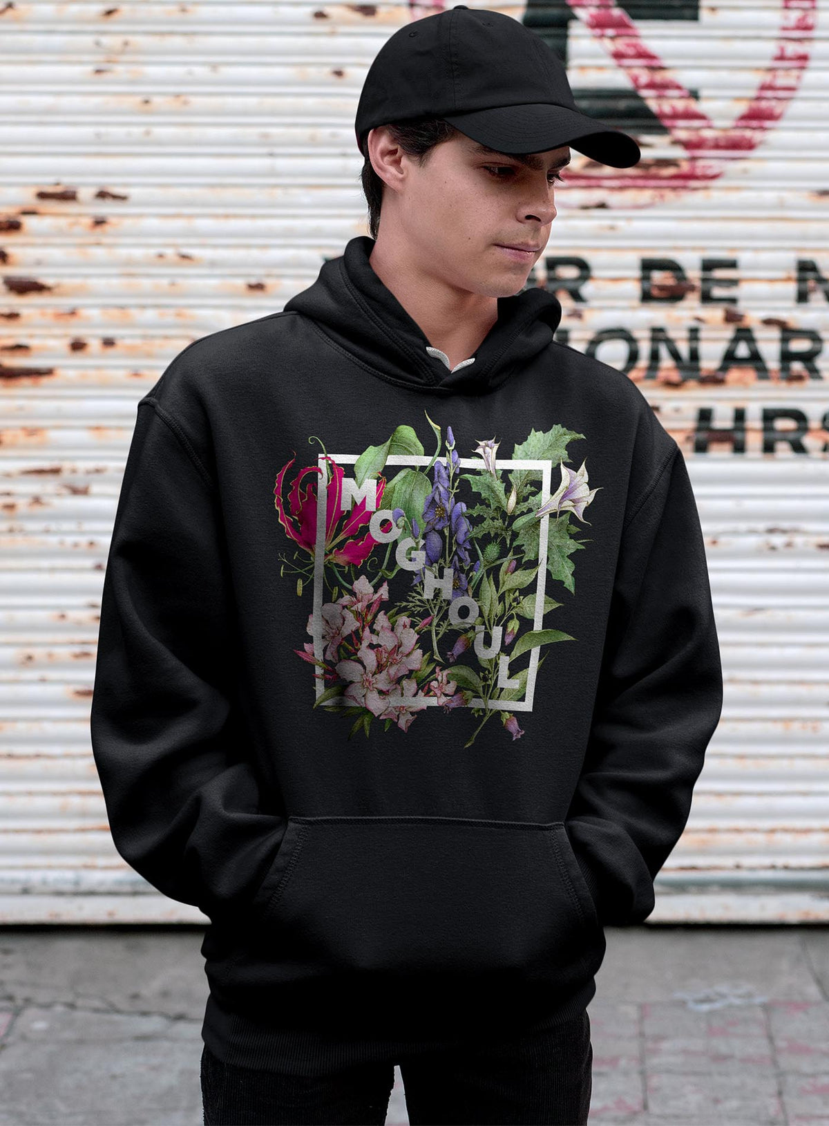 man modeling a Black unisex hoodie featuring white Moghoul logo surrounded by poisonous flowers such as oleander, fire lily, belladonna and toloache.