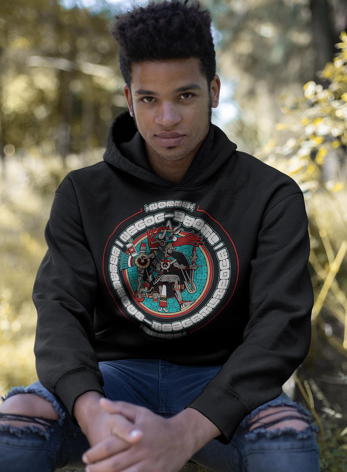Man modeling a black unisex hoodie featuring a front print of the toltec-aztec god Yayauhqui-Tezcatlipoca also known as Necoc-yaotl. Reinterpretation by Mexican illustrator G.M. Meave.