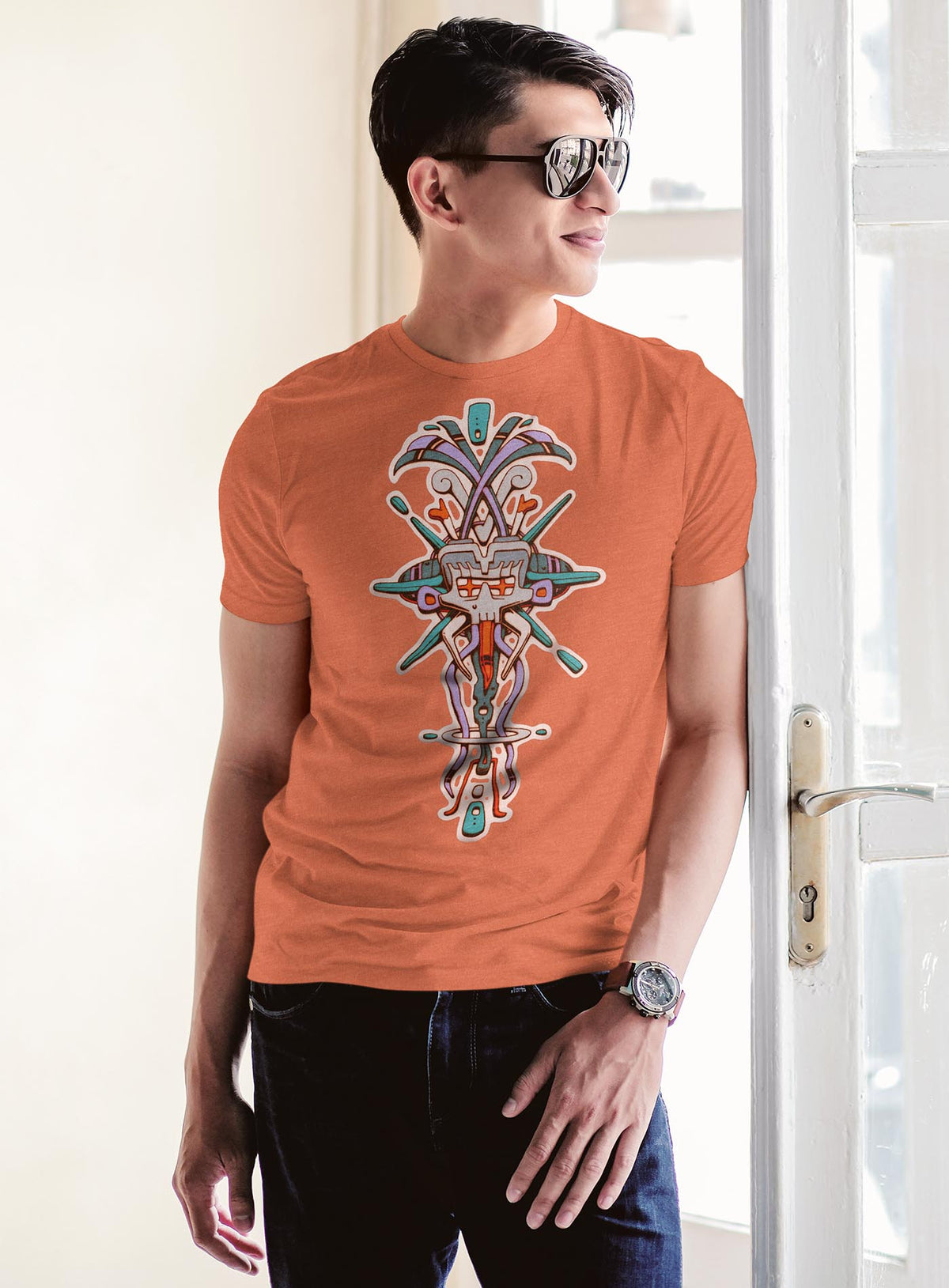 Man modeling a Heather orange unisex t-shirt featuring a front print of Tzontecotl, the Nahua word for skull, associated with a mask that submerged the wearer into the underworld. illustrated by G.M. Meave.