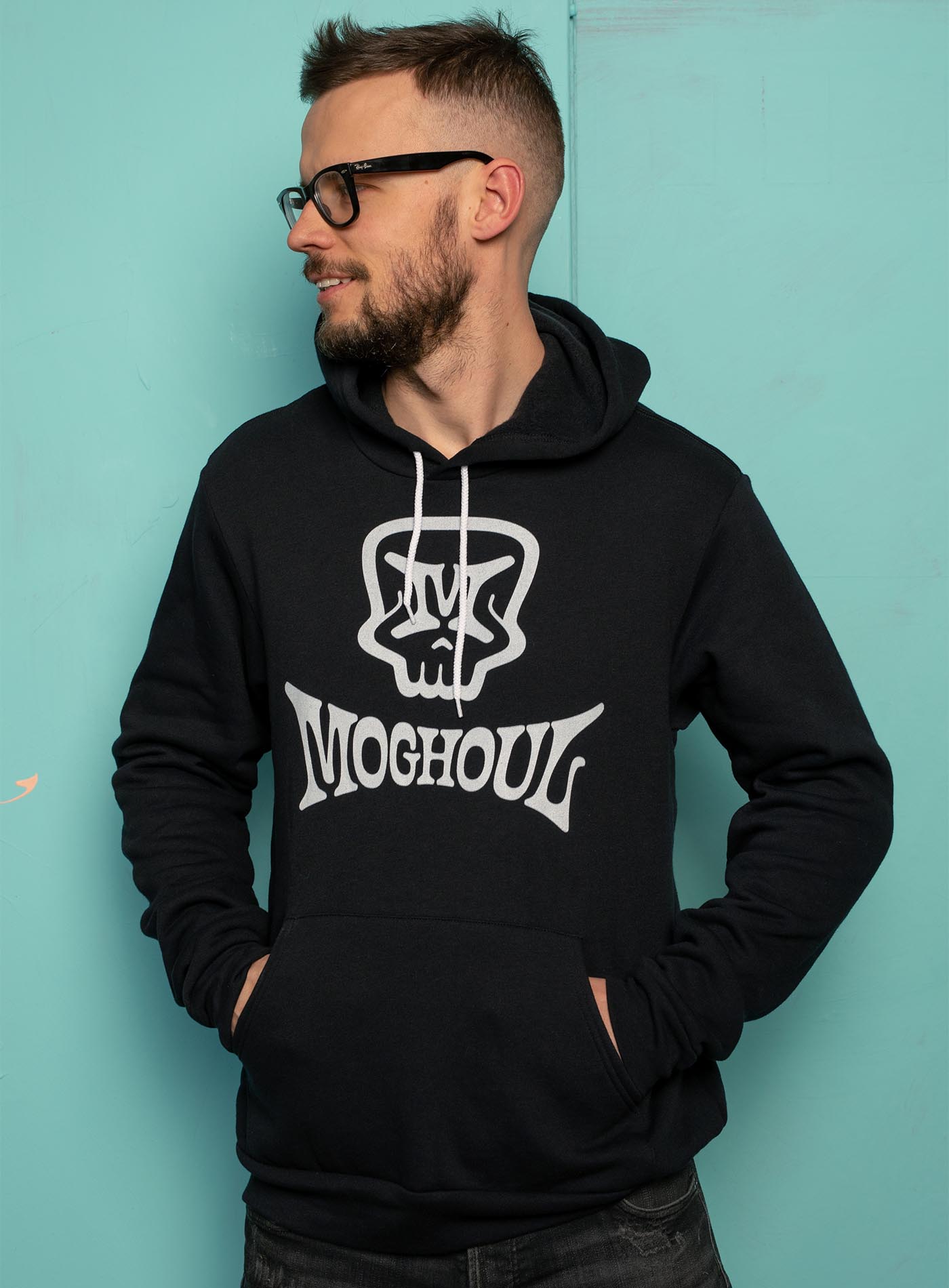 Female modeling a Black unisex hoodie featuring a front print of the Mr. M Moghoul logo by G.M. Meave.