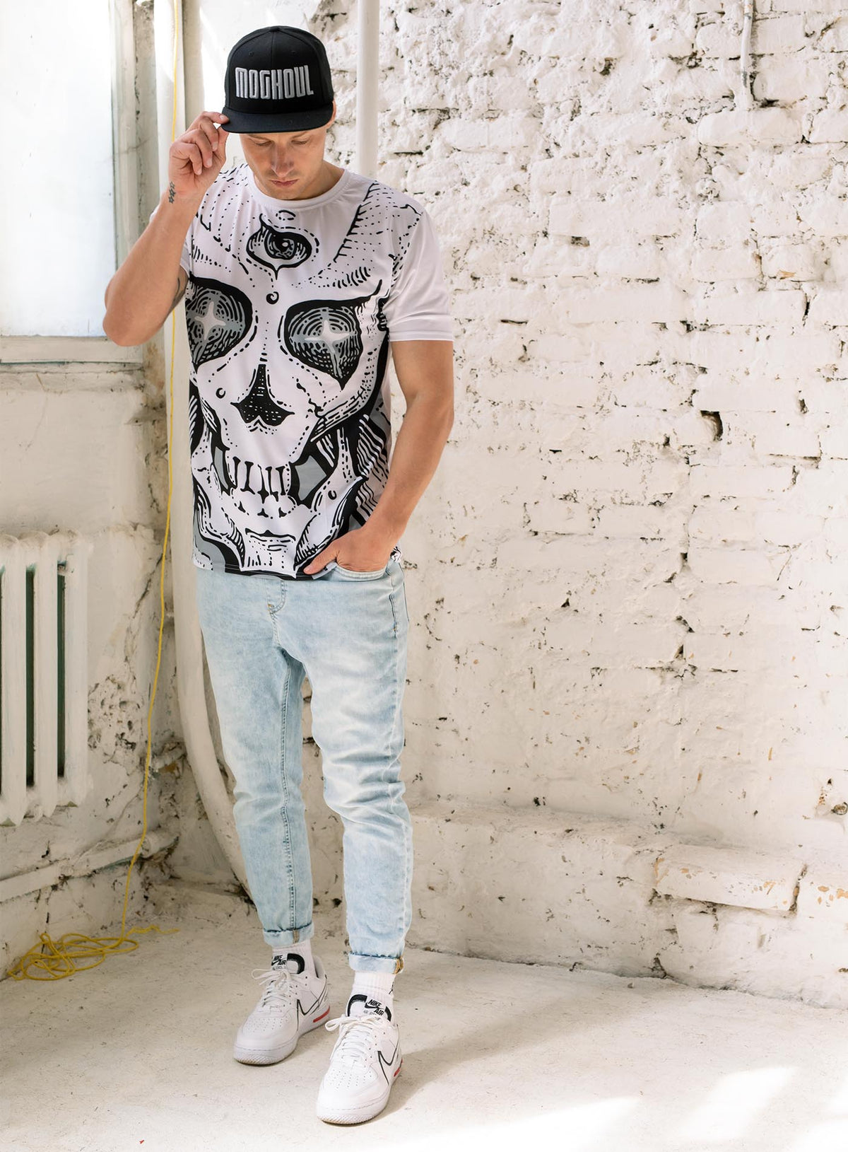 Man modeling an All over dye sublimation t-shirt featuring a front print of a three-bone alien Jolly Roger pirate illustration by G.M. Meave.