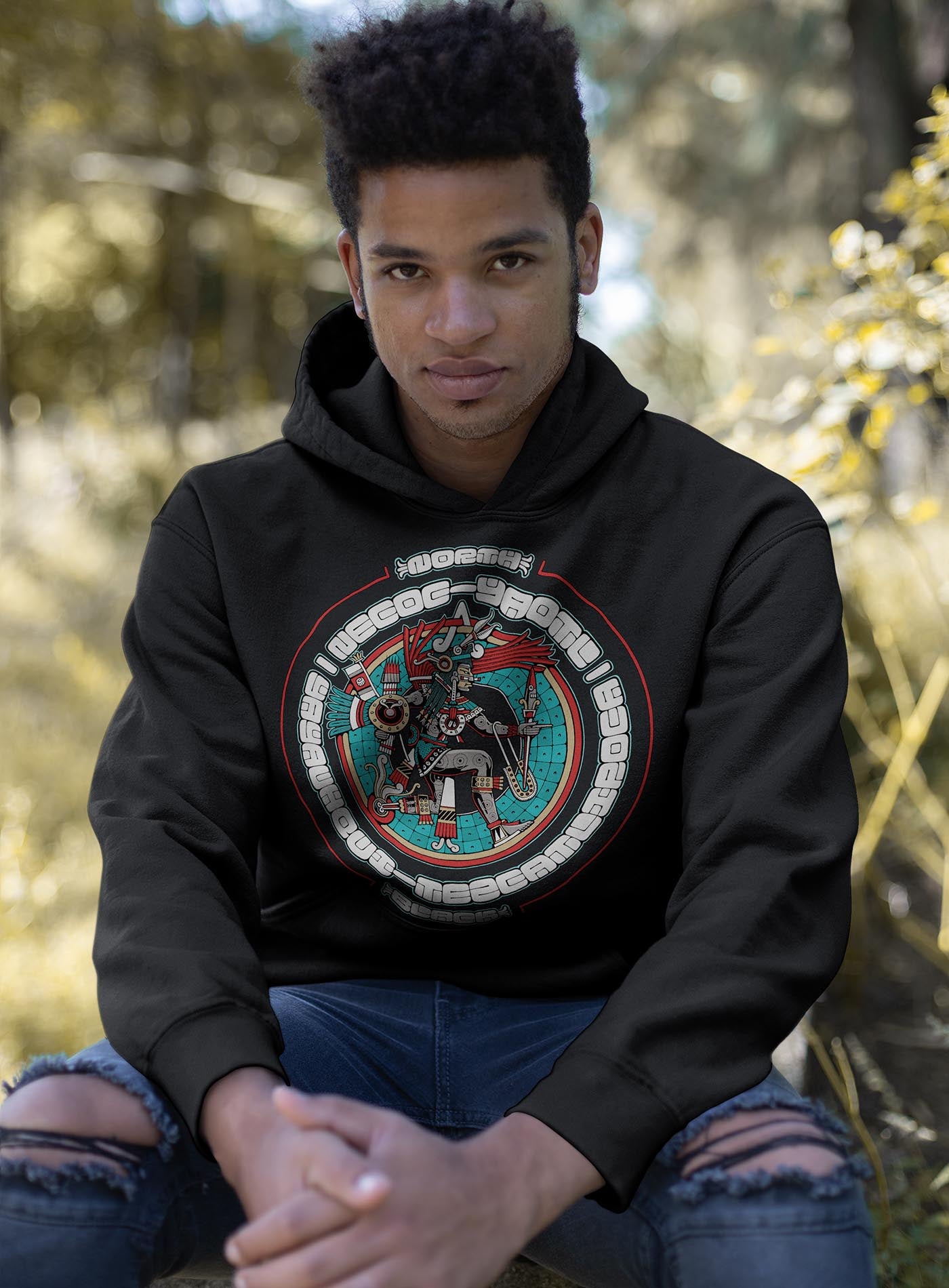 man modeling a black unisex hoodie featuring a front print of the toltec-aztec god Yayauhqui-Tezcatlipoca also known as Necoc-yaotl. Reinterpretation by Mexican illustrator G.M. Meave.