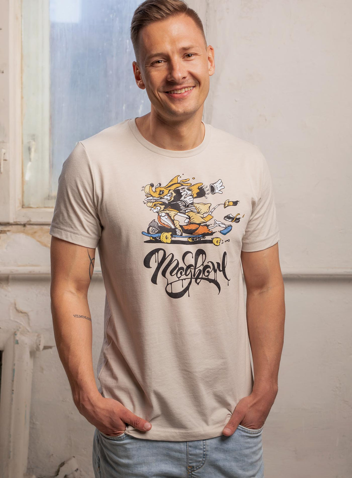 man modeling a heather beige  unisex t-shirt featuring a front print of Doom Dawg by street artist Chairman Ting, and the Moghoul logo.