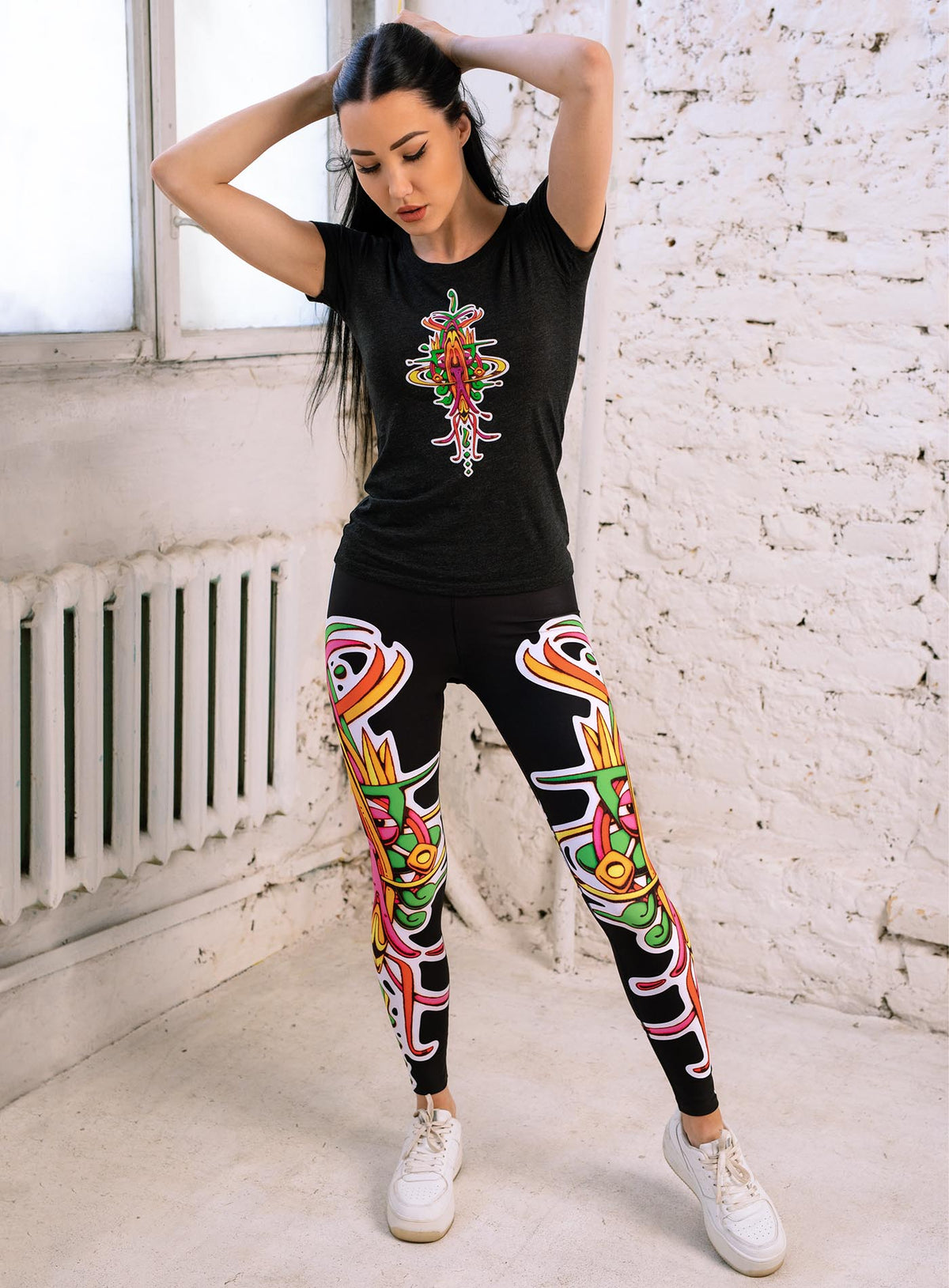 Woman modeling a Black woman&#39;s t-shirt and all over dye sublimation leggings featuring a front print of the Toltec-Aztec hummingbird deity illustrated by G.M. Meave.