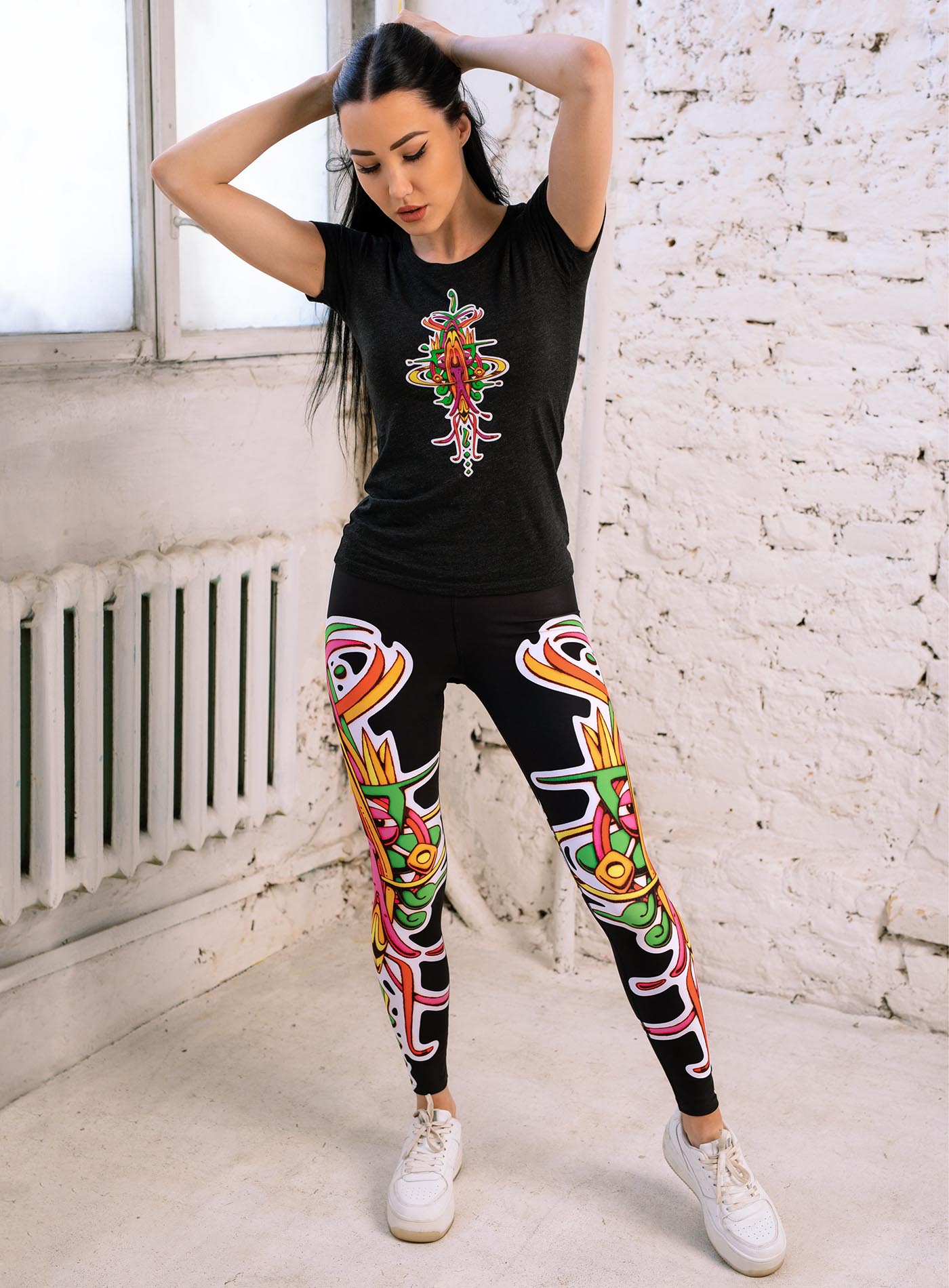 Woman modeling a Black woman's t-shirt and all over dye sublimation leggings featuring a front print of the Toltec-Aztec hummingbird deity illustrated by G.M. Meave.