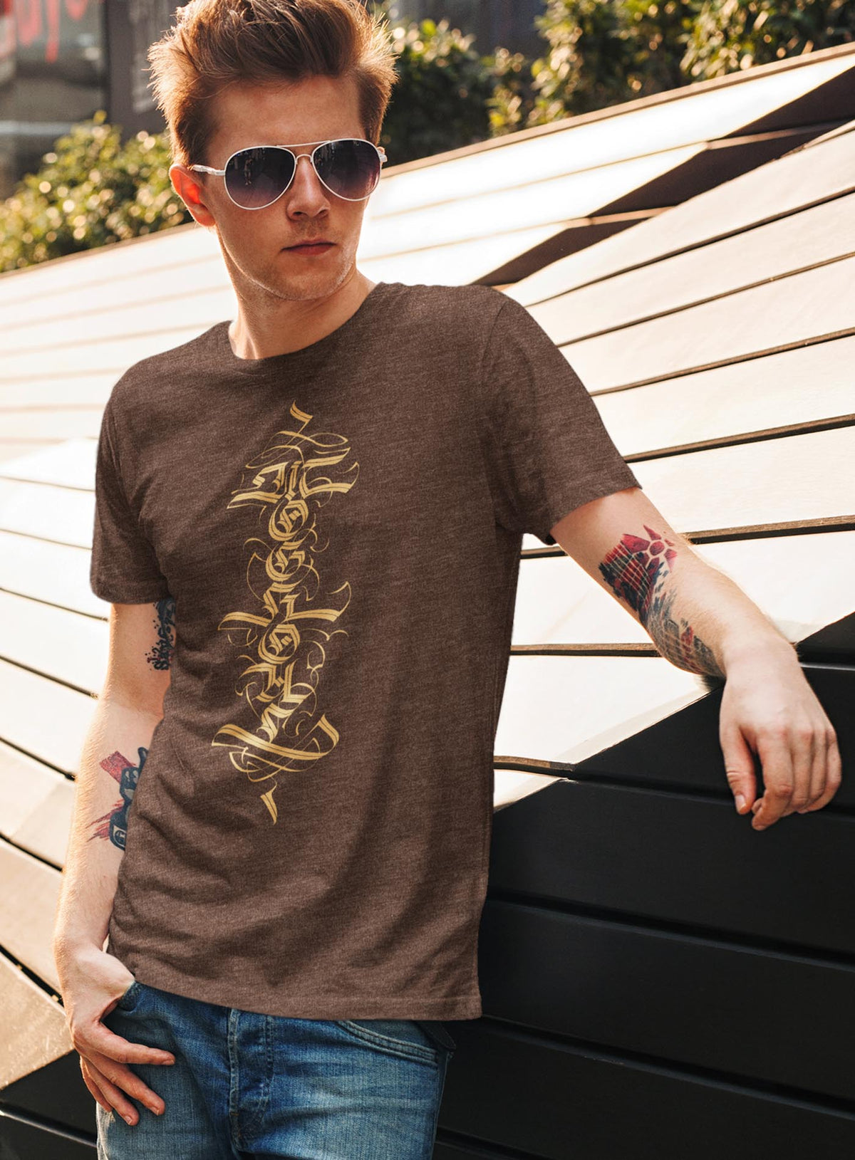 Man modeling a Heather brown unisex t-shirt featuring a front print of a white Moghoul straight-up-gothic logo by Mexican typographer G.M. Meave.