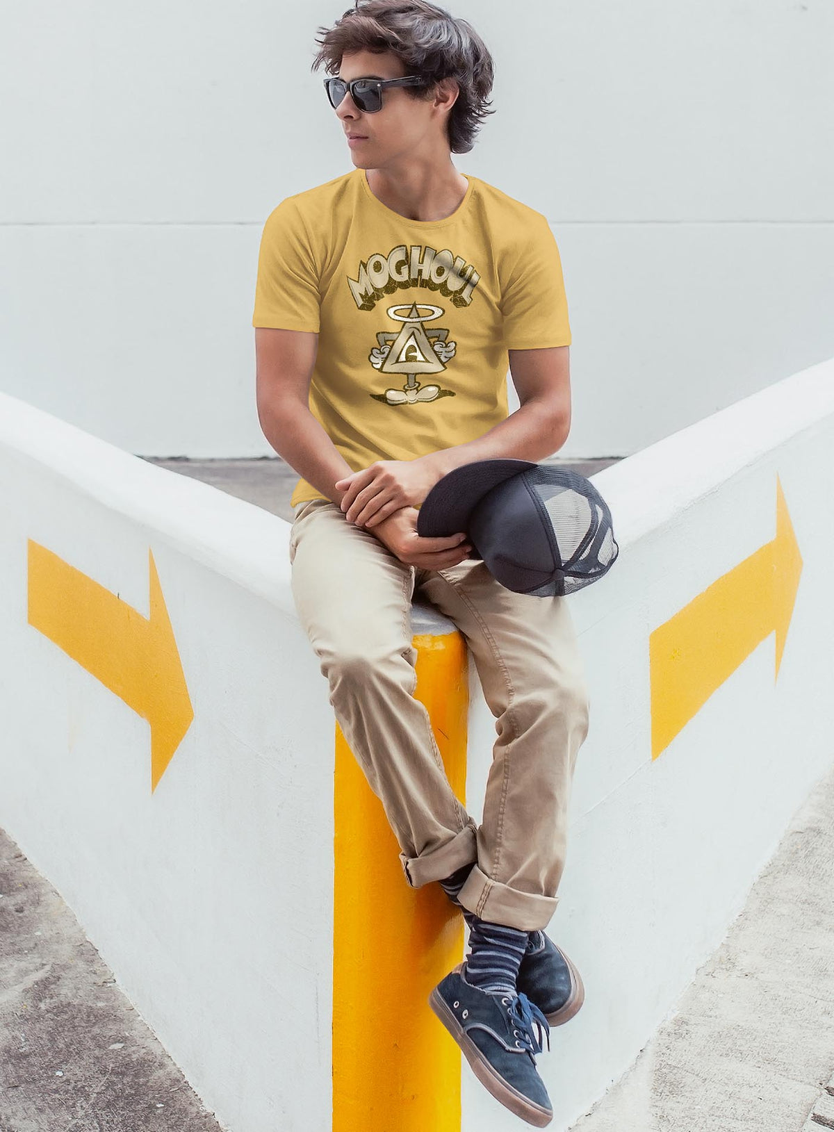 Man modeling a yellow unisex t-shirt featuring a front print of a cartoon character based on the mythical Eye of Providence. By Mexican illustrator G.M. Meave