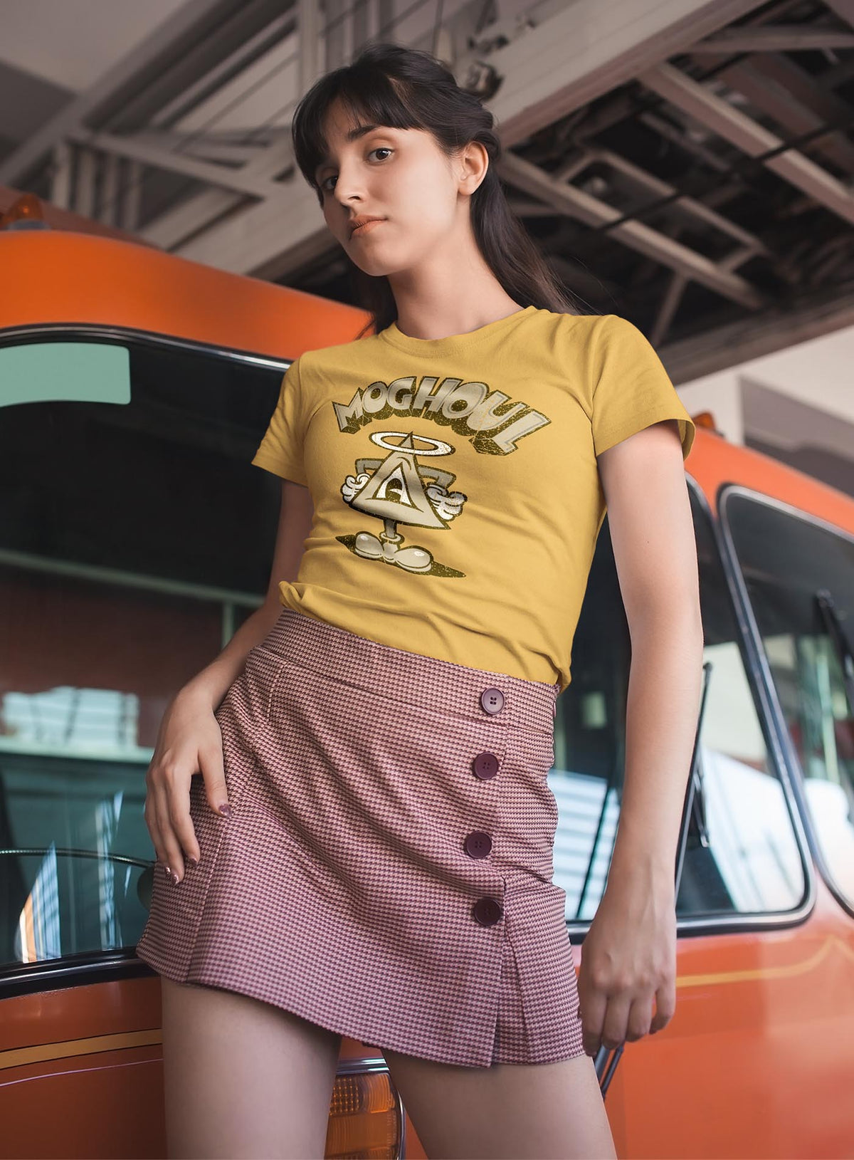 Woman modeling a yellow unisex t-shirt featuring a front print of a cartoon character based on the mythical Eye of Providence. By Mexican illustrator G.M. Meave