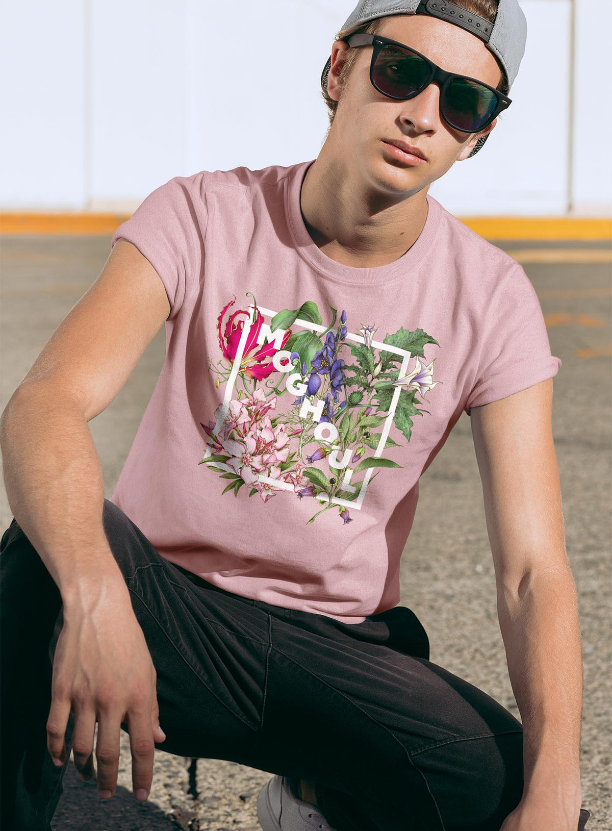 Man modeling a Pink unisex t-shirt featuring white Moghoul logo surrounded by poisonous flowers such as oleander, fire lily, belladonna and toloache.