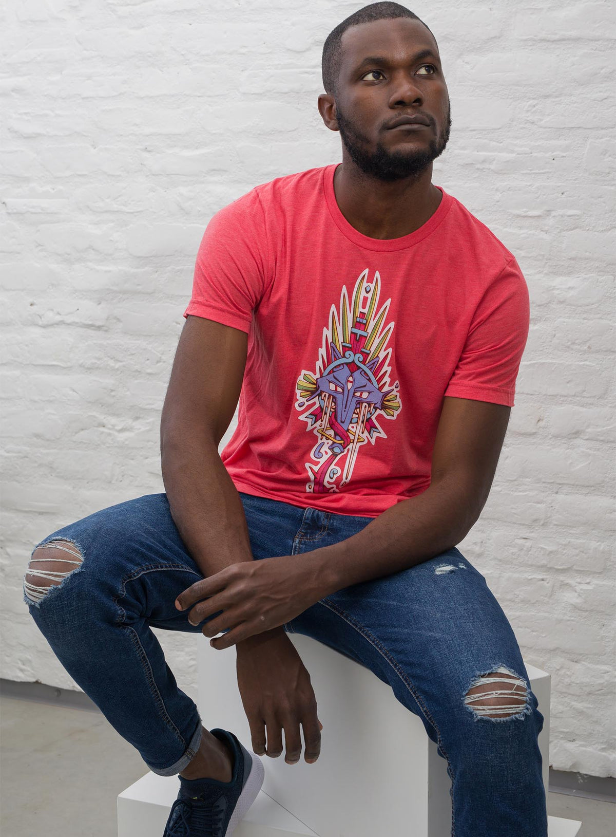 Man modeling a heather red unisex t-shirt featuring a front print of the Toltec and Aztec coyote deity illustrated by G.M. Meave