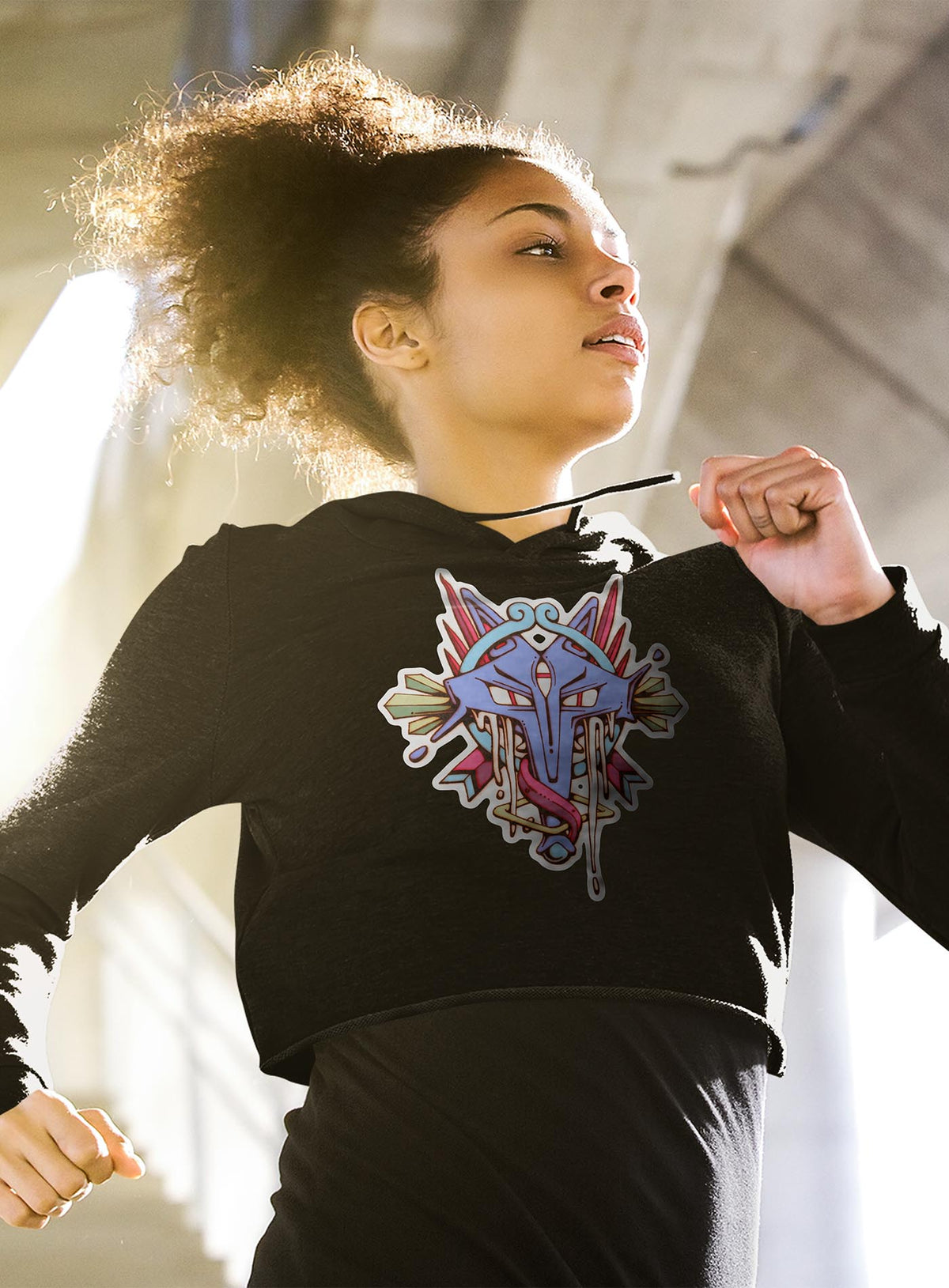 Woman modeling a Black woman&#39;s cropped hoodie featuring a front print of the Toltec and Aztec coyote deity illustrated by G.M. Meave.